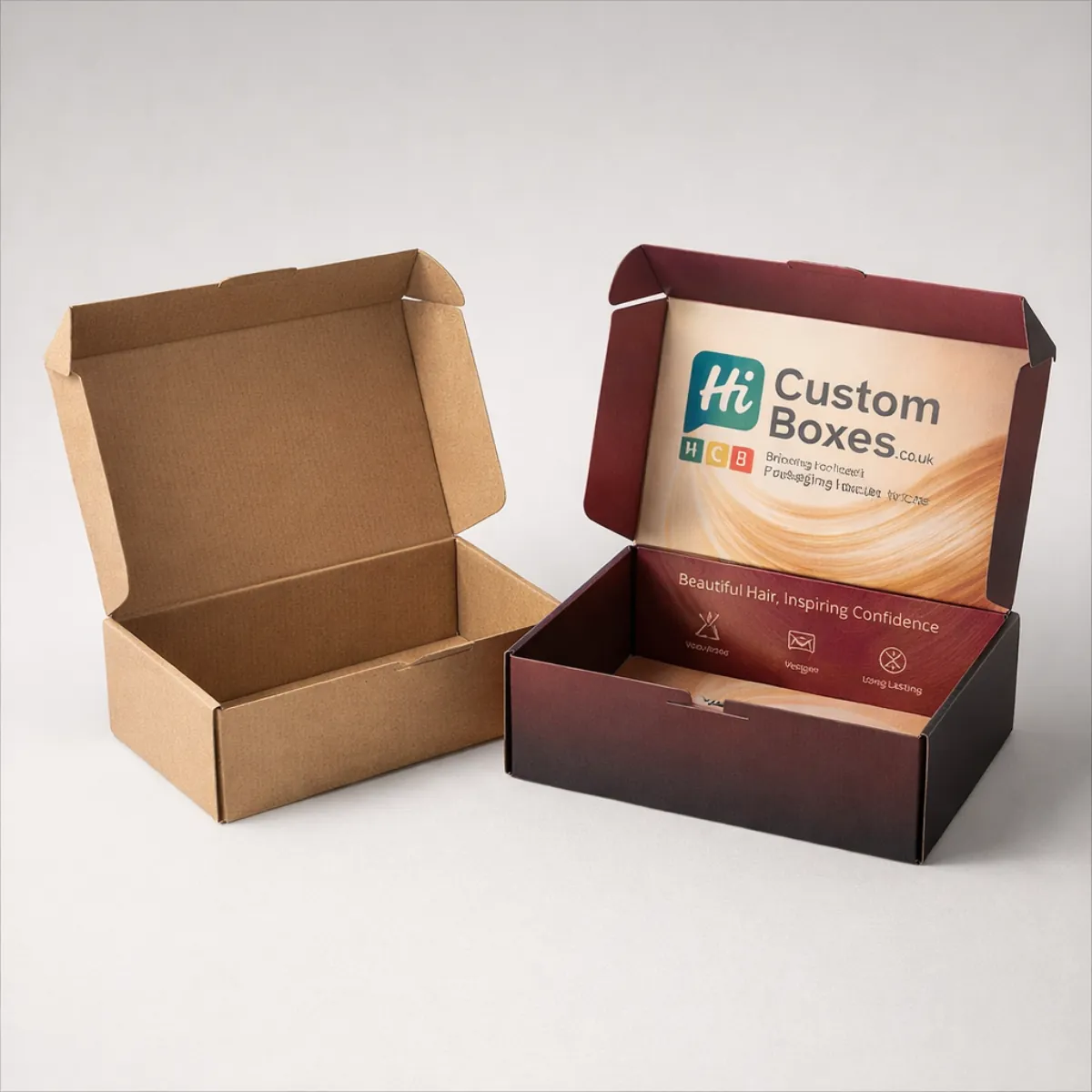 An open kraft mailing box beside a custom burgundy mailer box with interior branding and slogans. class=